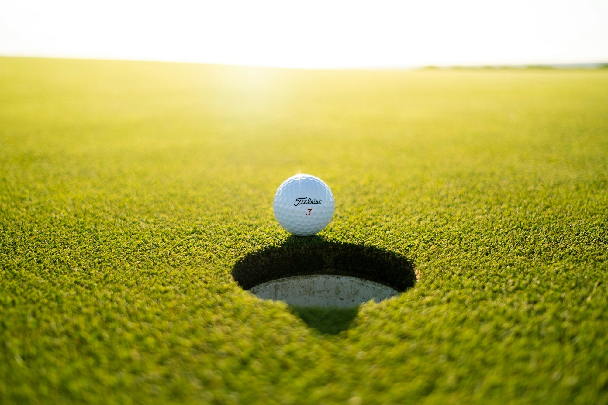 Golfball am Rand eines Lochs auf einem Grün im Gegenlicht