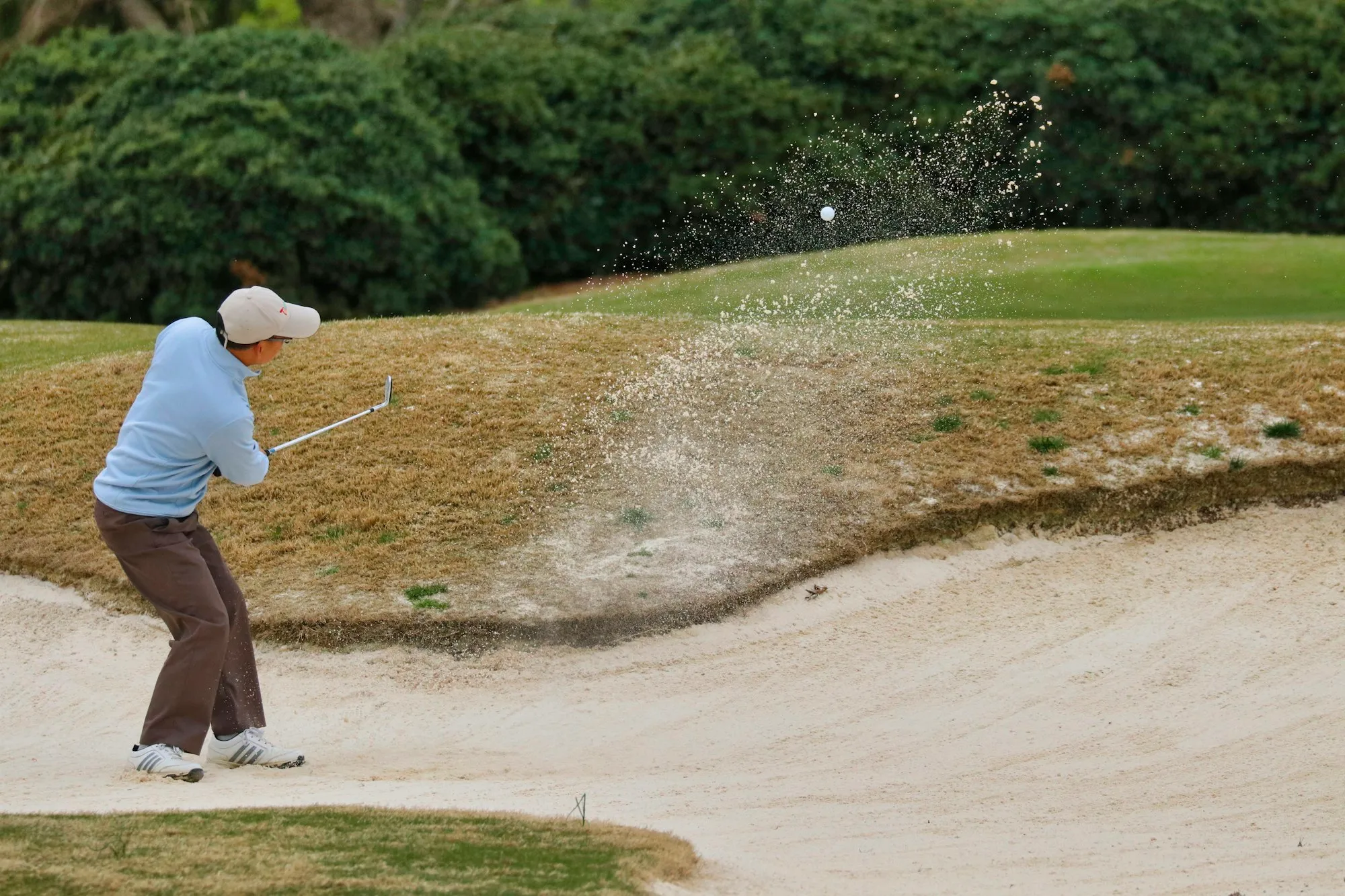Golfer schlägt mit offenem Schlägerblatt aus dem Sandbunker