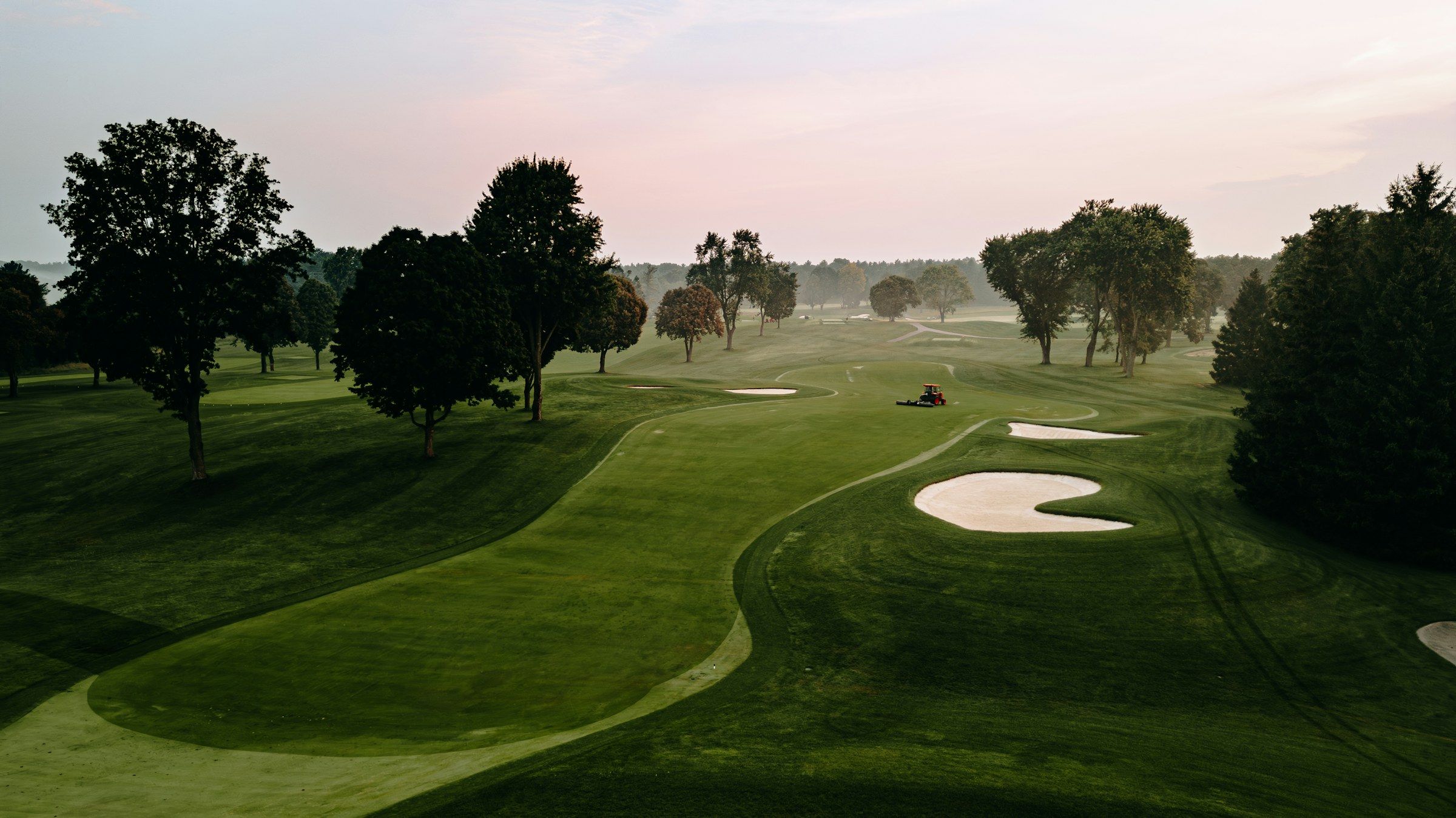 Weitläufiger Golfplatz im Morgenlicht mit geschwungenen Fairways, Bunkern und Baumgruppen