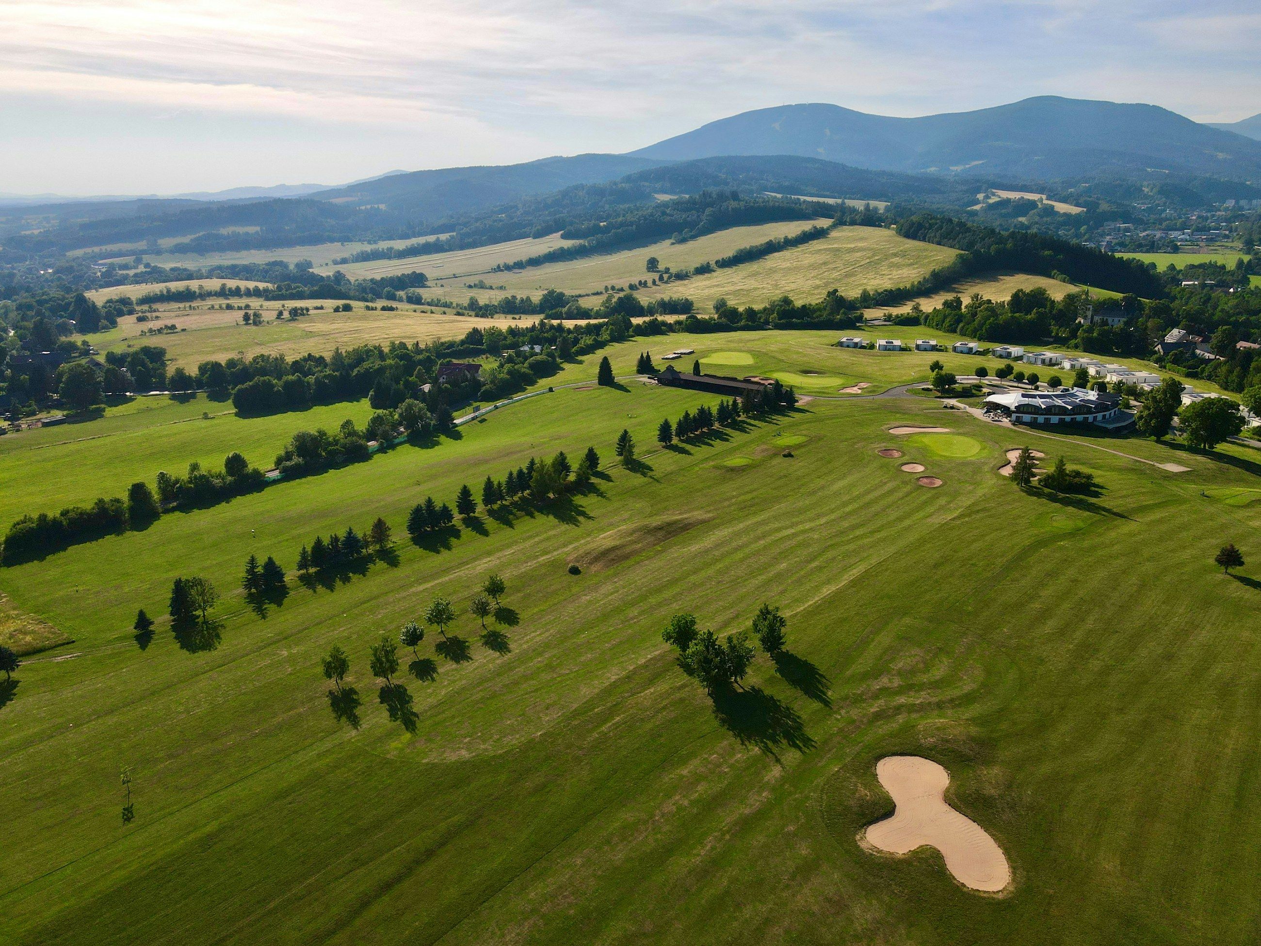 Luftaufnahme eines Golfplatzes in hügeliger Landschaft mit Clubhaus und Bergen im Hintergrund