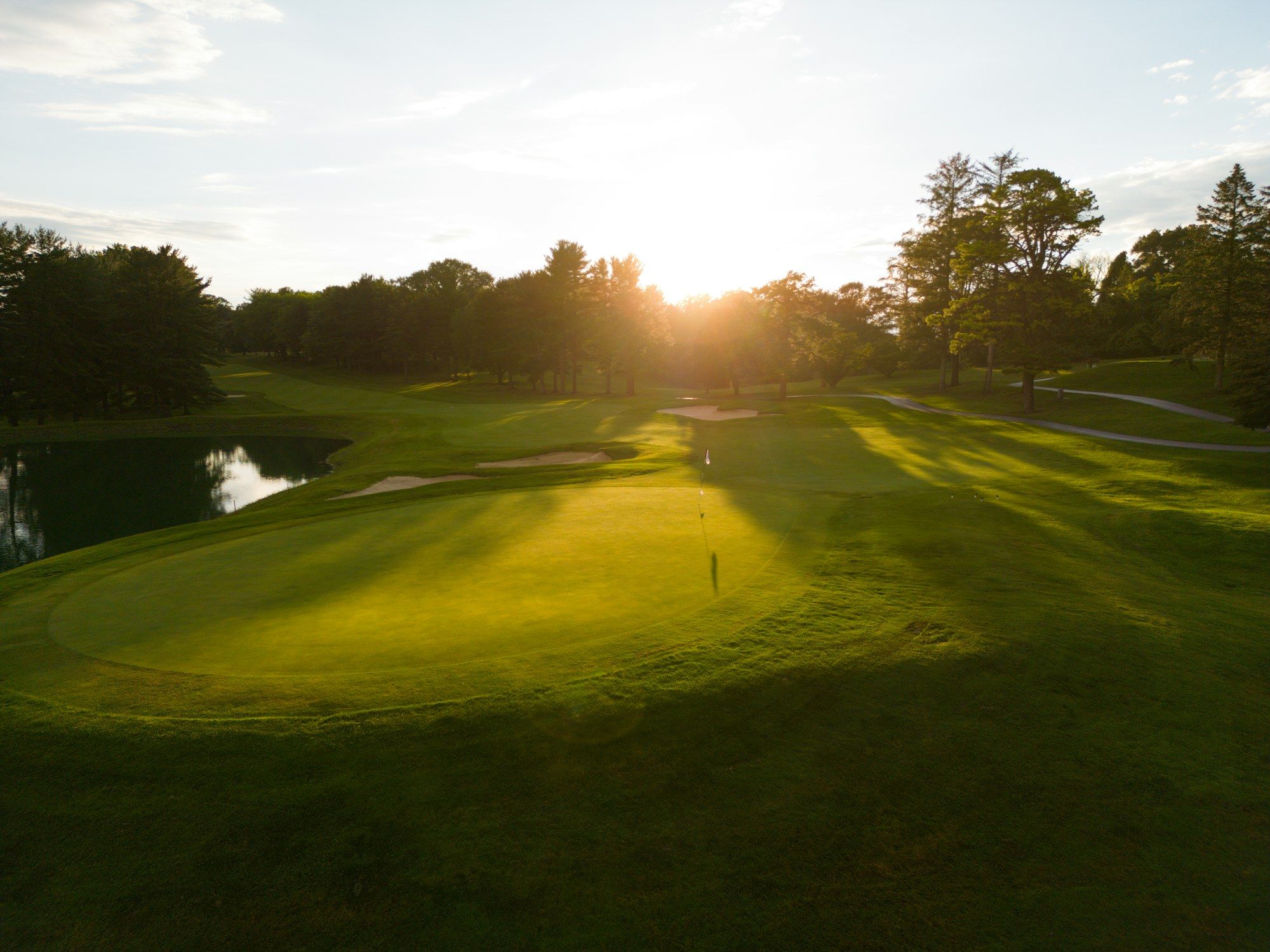 Grün eines Golfplatzes im Morgenlicht mit Fahne und Bäumen im Hintergrund