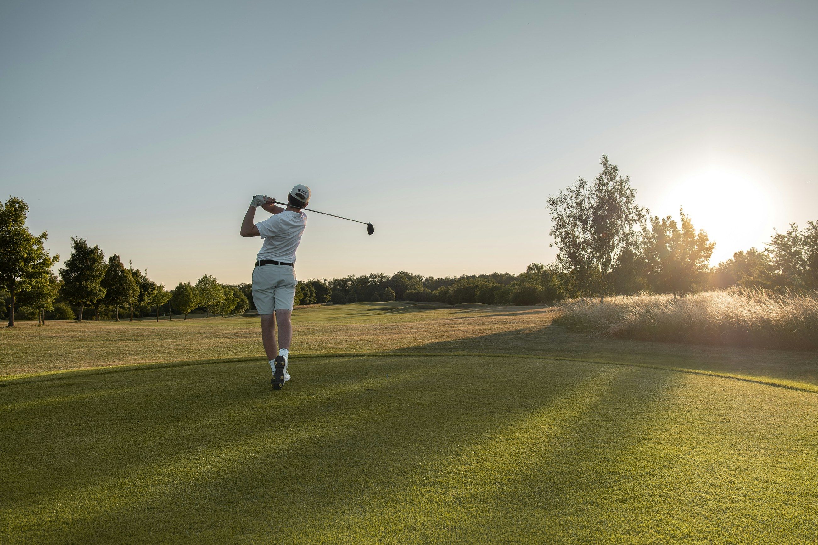 Golfer im Finish seines Abschlags auf einem Abschlag bei tiefstehender Sonne
