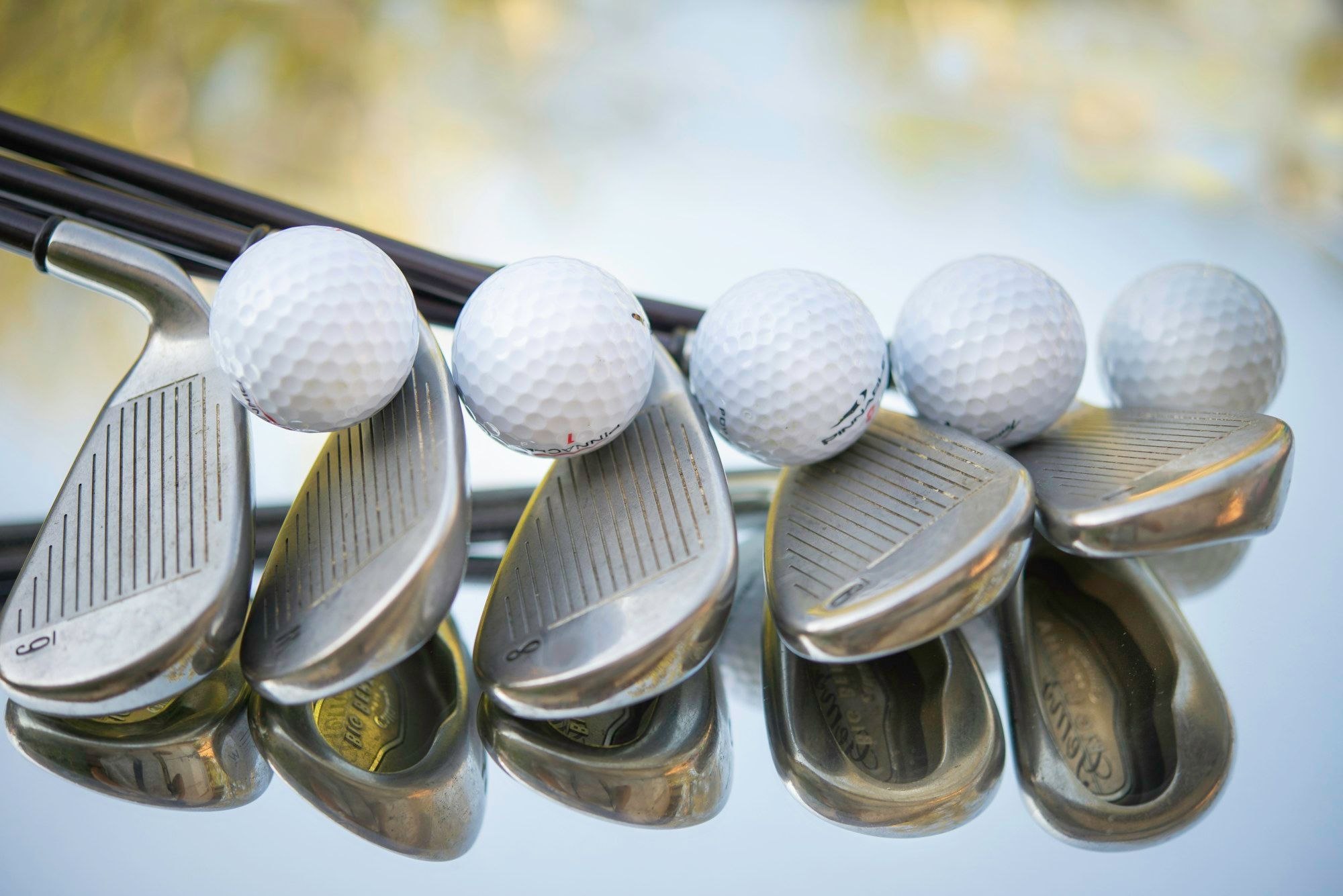 Fünf Eisen mit der Schlagfläche nach oben, auf jedem liegt ein weißer Golfball