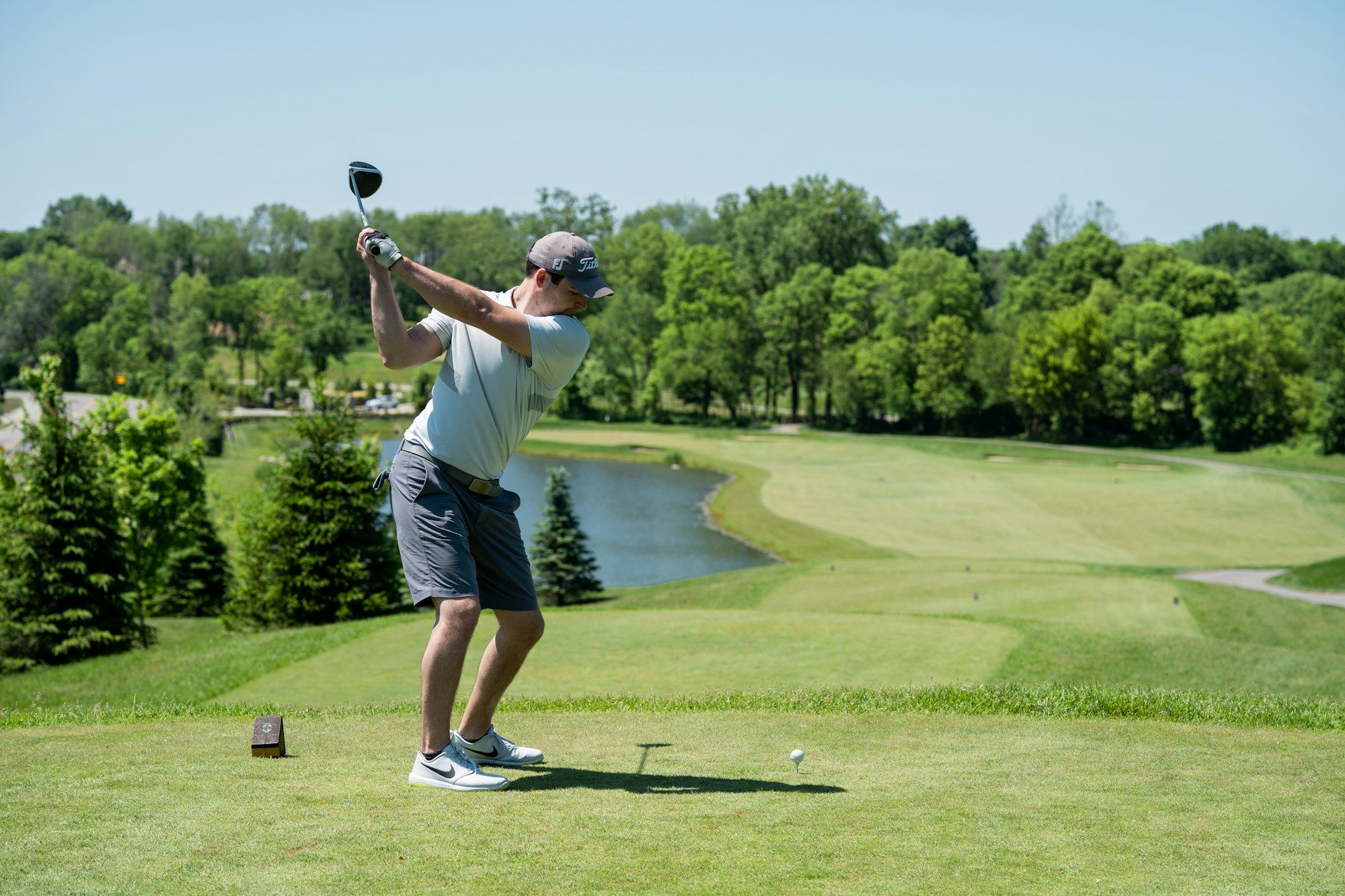 Golfer beim Abschlag auf einem Fairway mit Bäumen im Hintergrund
