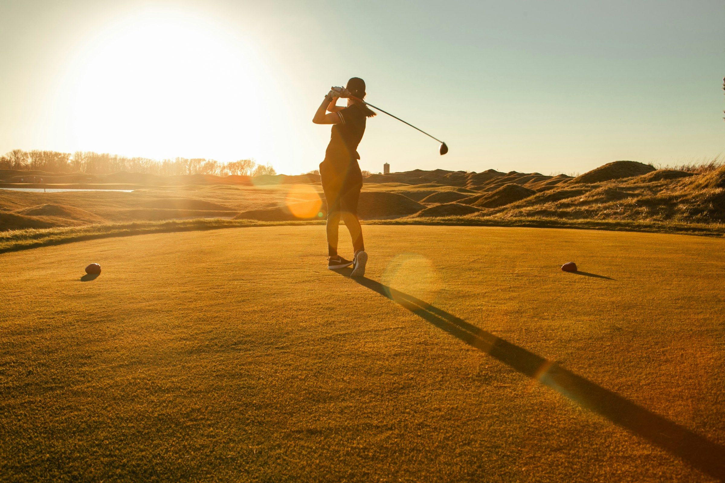 Golfer beim Schwung auf dem Übungsgelände bei tiefstehender Sonne